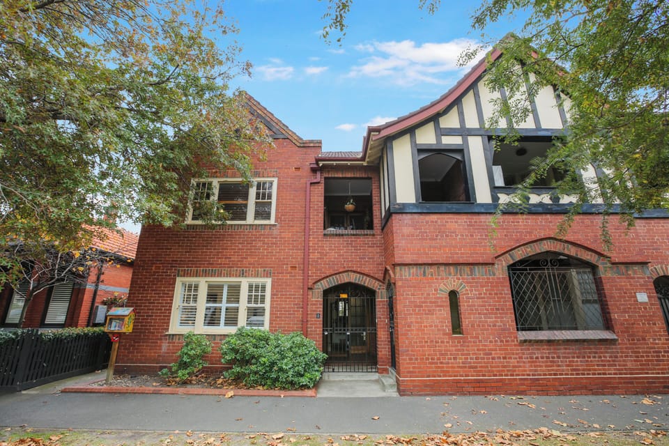 Charming brick Tudor residence with arched entry, balcony, and leafy setting