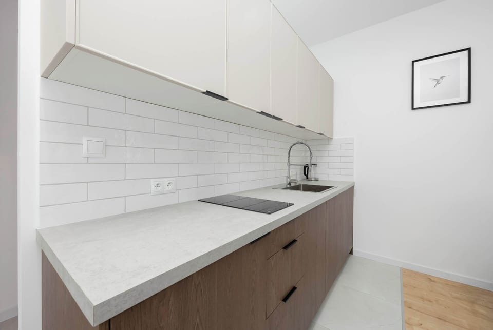 An angled view of the kitchenette reveals a gray countertop fitted with a built-in electric cooktop. The clean white tiled wall features a single framed piece of minimalist graphic art.