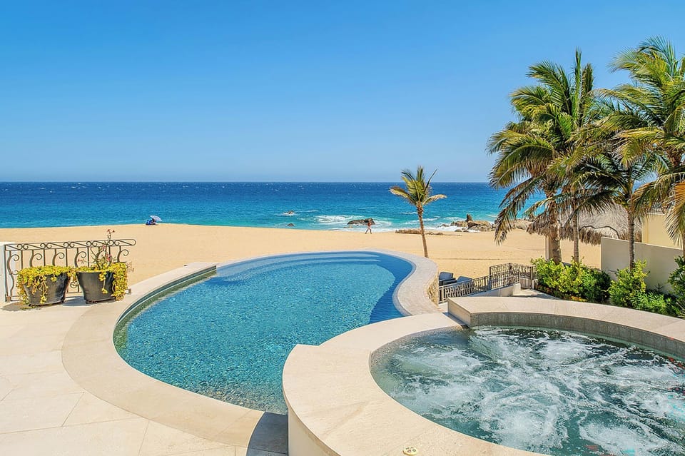 Beachfront property featuring a private swimming pool and hot tub overlooking pristine golden sands and turquoise ocean waters, framed by swaying palms.