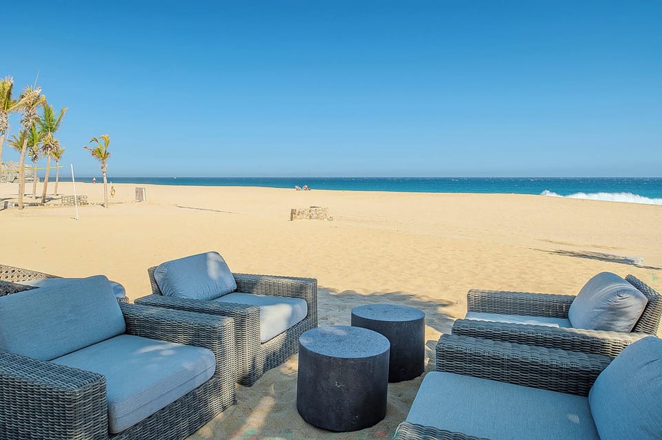 Private beachfront lounge featuring wicker seating with plush blue cushions set on golden sand, where turquoise waves meet endless blue skies and swaying palms frame your oceanfront escape.