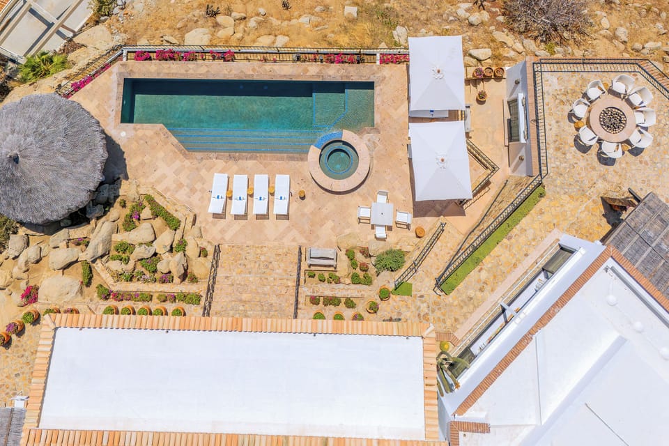 Aerial view of the property showcasing a pristine swimming pool, hot tub, outdoor dining areas, and landscaped grounds with mountain terrain backdrop.
