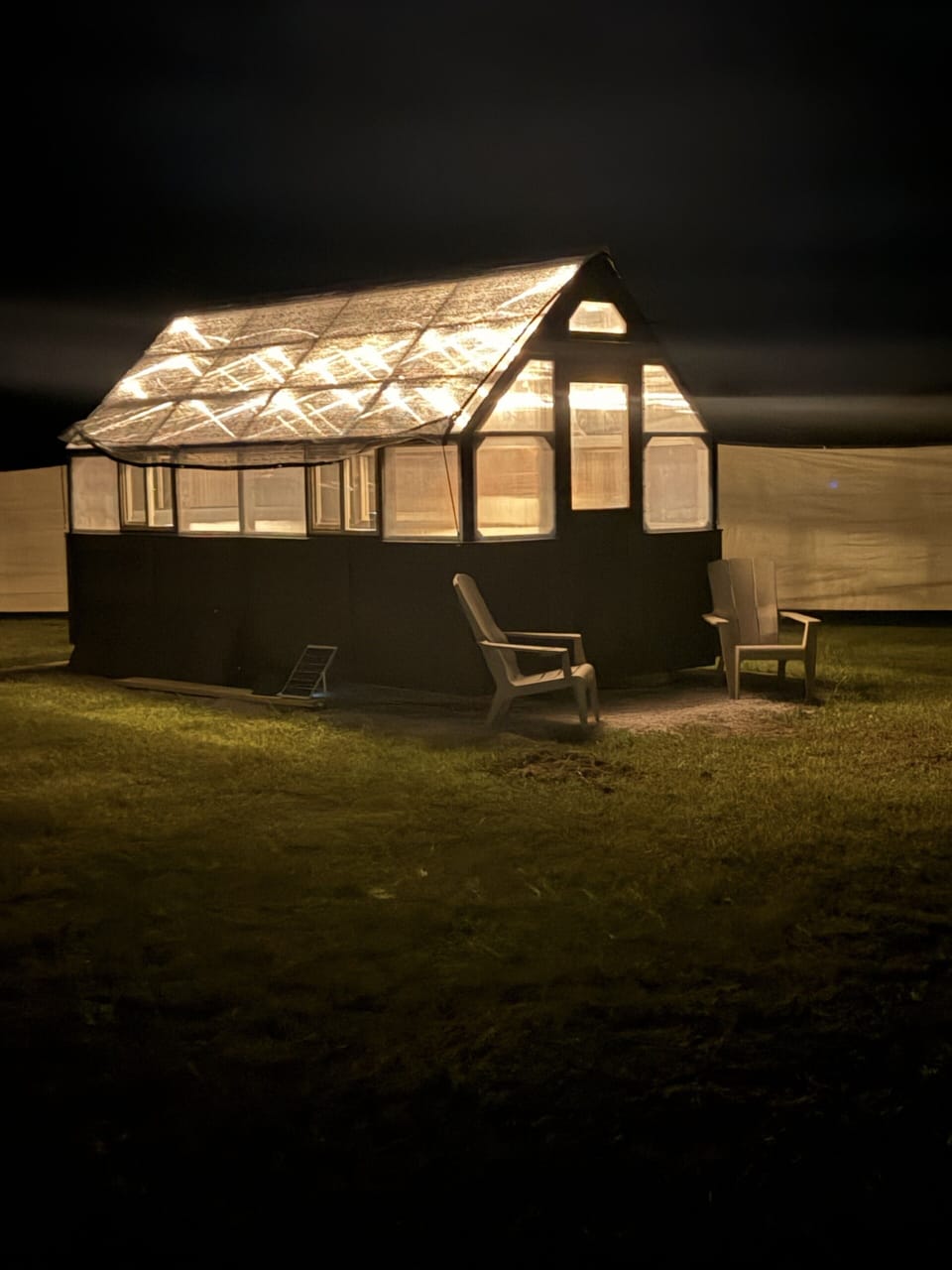 Glowing greenhouse-style cabin with cozy seating under the night sky