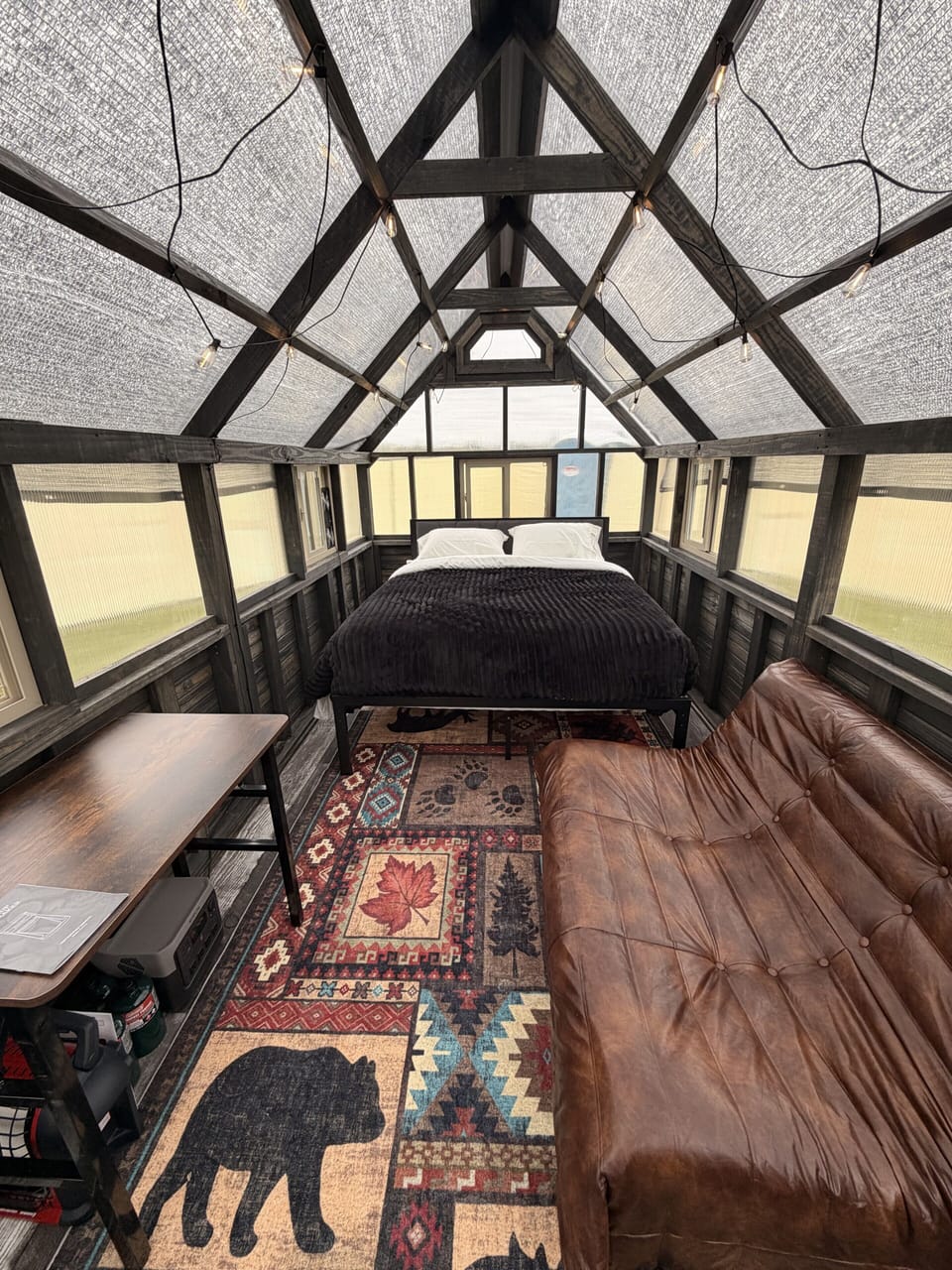 Cozy glass-roof cabin nook with plush bed, leather sofa, and rustic charm