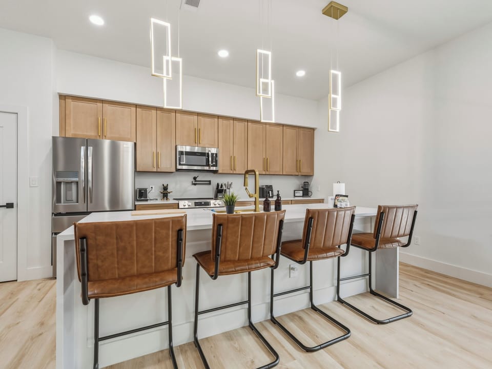 Picture yourself here in this bright open kitchen, gathering at the island with modern pendant lighting above. Sleek stainless appliances, warm wood cabinetry, and stylish seating make meal prep a delight.