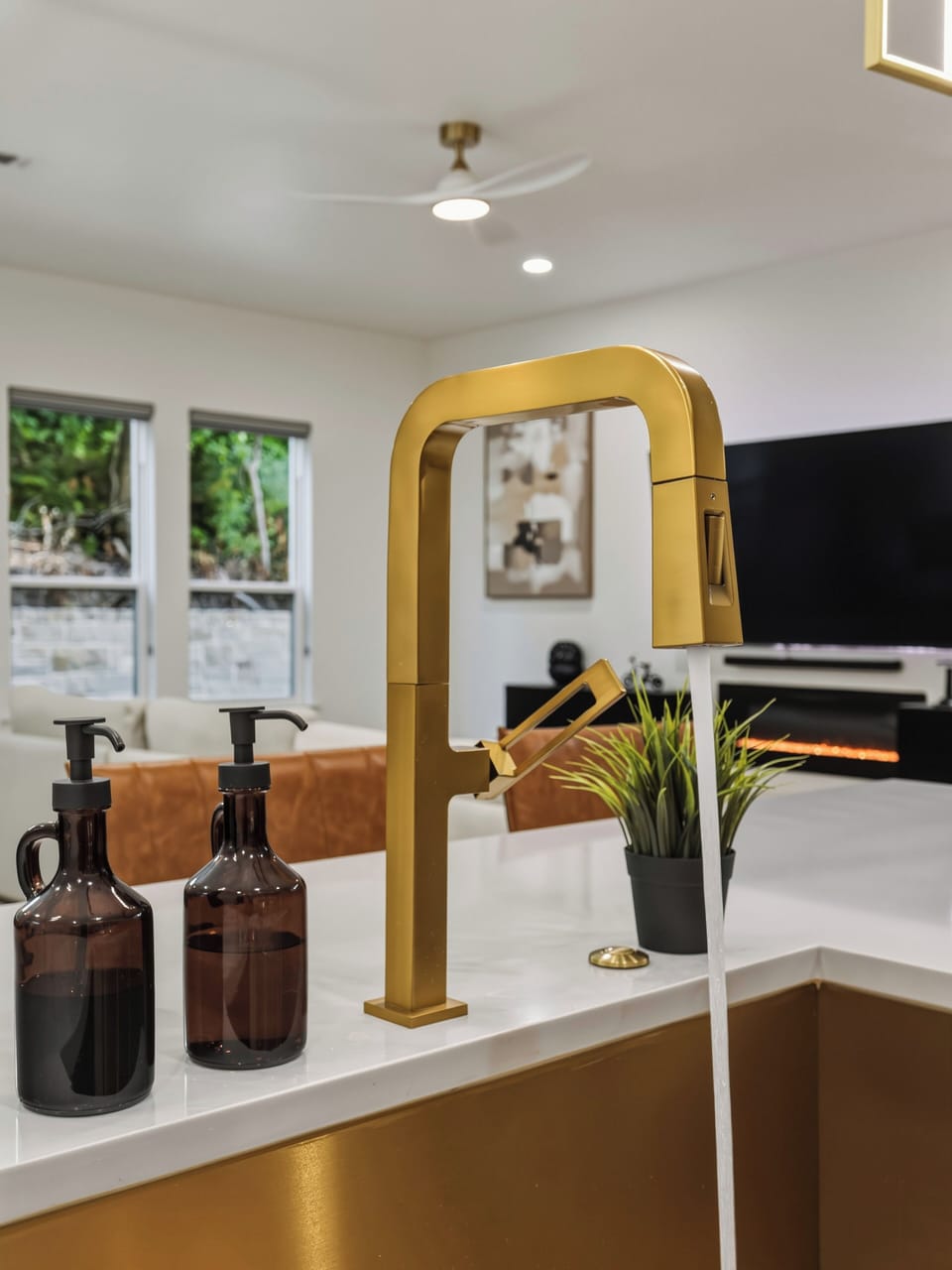 A stunning gold faucet and modern fixtures create an upscale kitchen centerpiece, complemented by stylish décor and glimpses of lush greenery outside your windows.