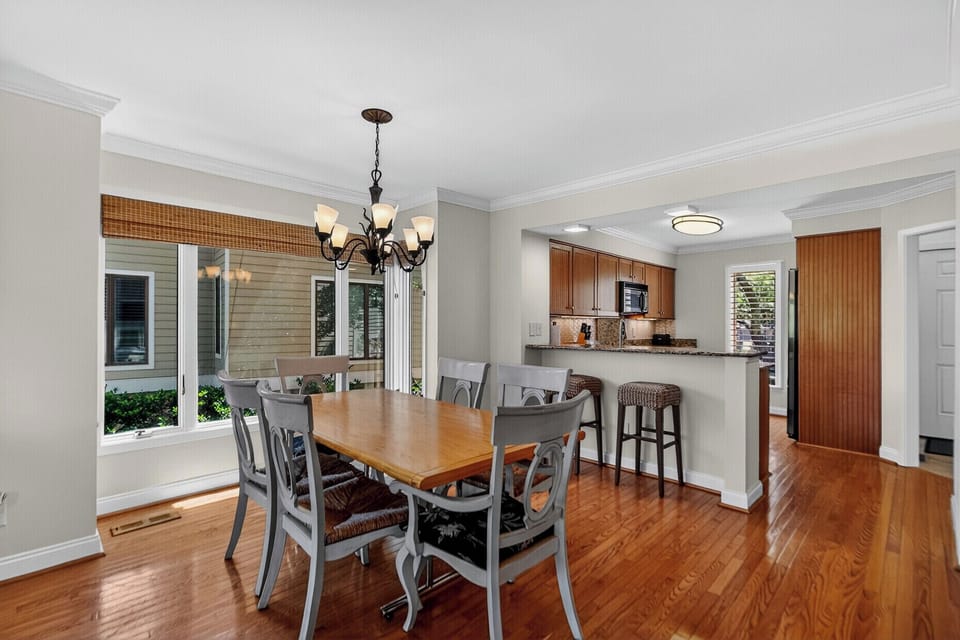 Your open-concept dining and kitchen space features gleaming hardwood floors, a breakfast bar for casual meals, and abundant natural light streaming through floor-to-ceiling windows overlooking the lush greenery outside.