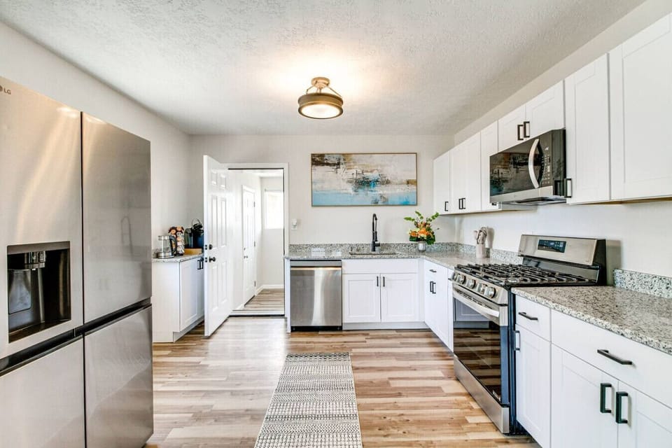 Open-concept kitchen with full appliance suite, gas range, white shaker cabinets, and granite counters — everything you need to cook a real meal together. Keurig and starter coffee ready to go.