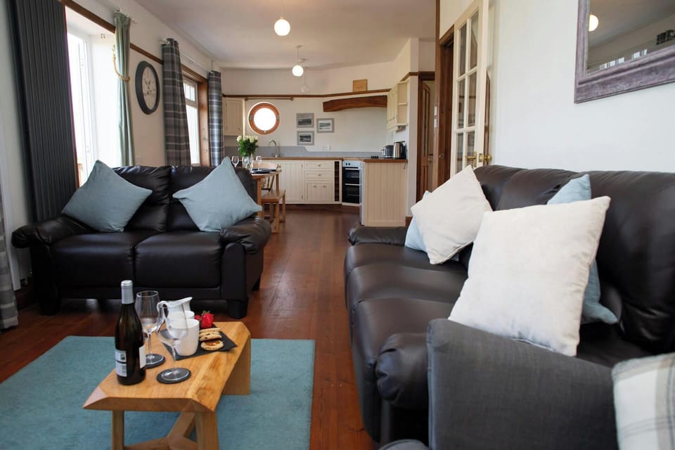 Open-plan living room with two black sofas and kitchen in the background