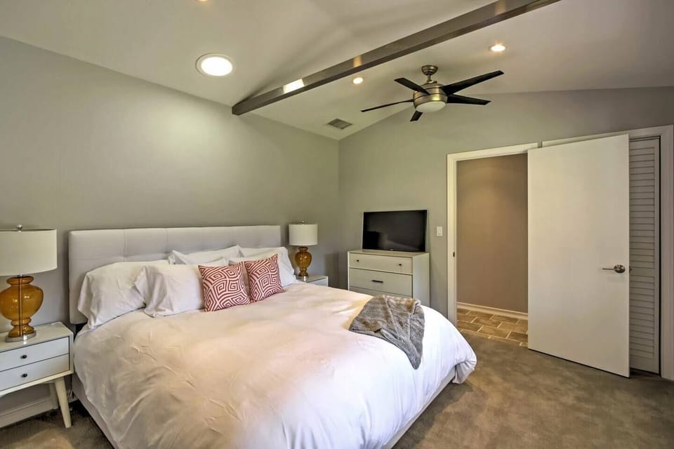 Cozy king bedroom with a vaulted beamed ceiling, modern ceiling fan, smart TV, and coral throw-pillow accents.
