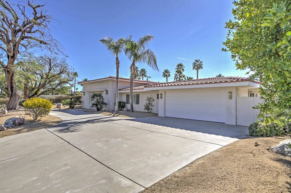 Single-story Spanish-style home with a red tile roof, attached two-car garage, and a wide concrete driveway lined with mature palms.