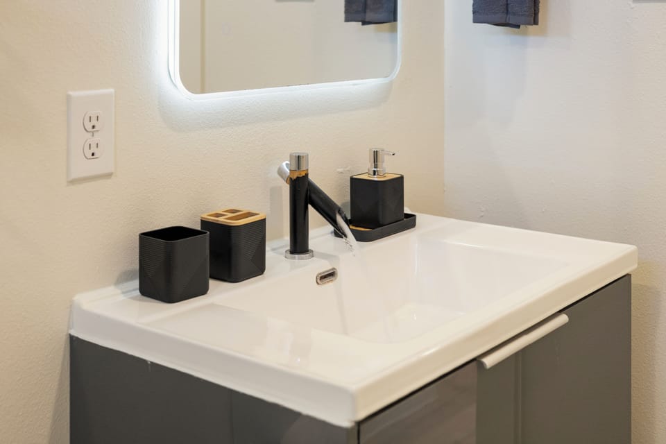 Modern bathroom vanity with a spacious sink, matte black faucet, illuminated mirror, and neatly arranged essentials for a clean and convenient daily routine.