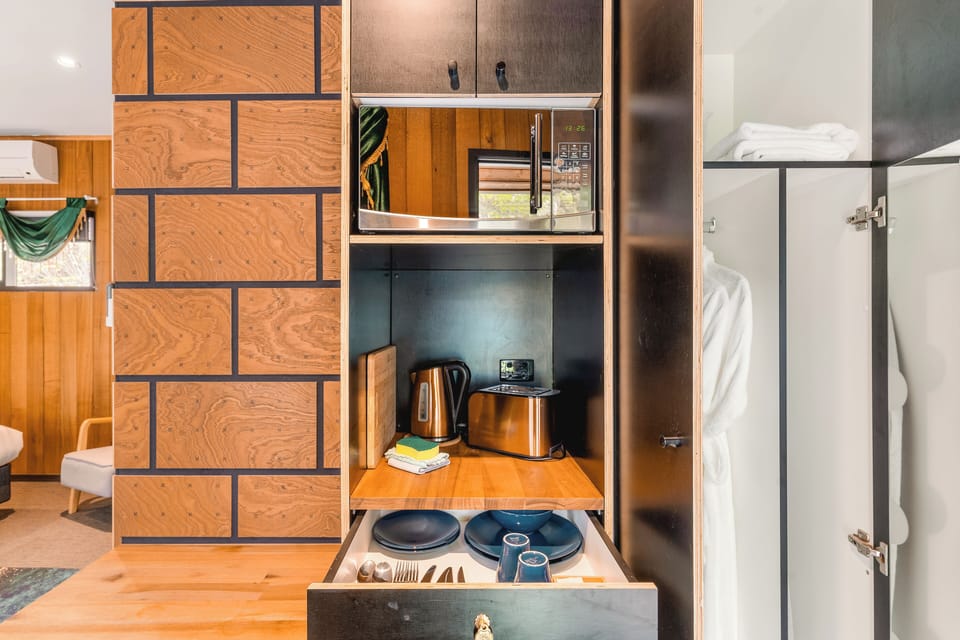 Compact kitchenette with microwave, kettle, toaster, and dishware—meal-ready.