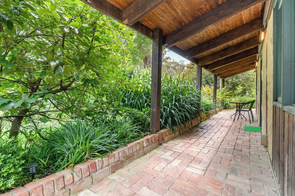 Shaded brick veranda amid lush gardens—rustic spot for morning coffee.