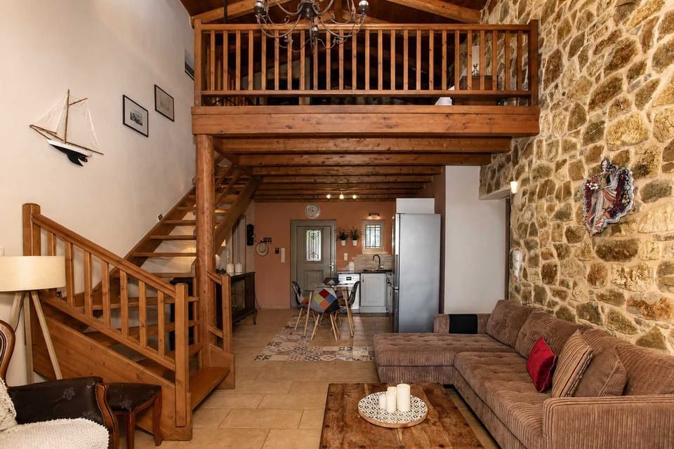 Double height living area with exposed stone walls, timber ceilings, and a loft overlooking the main space.