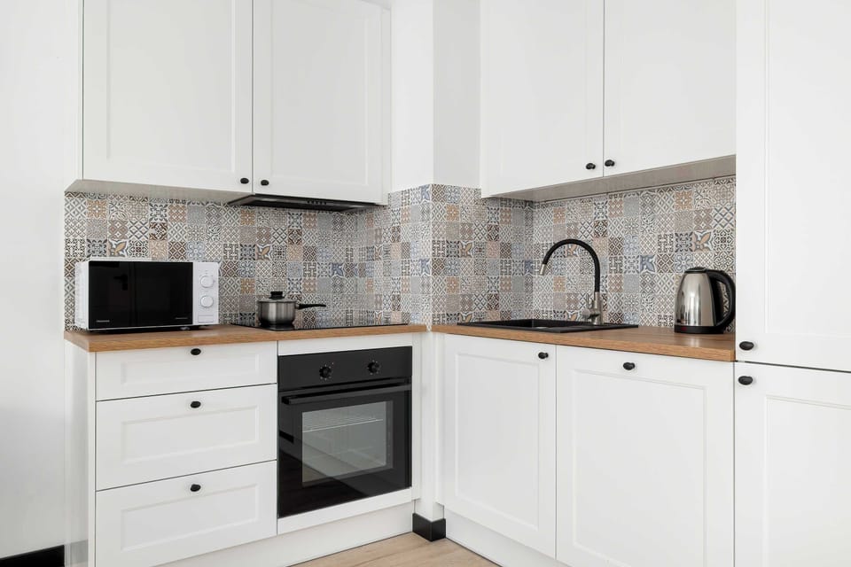 Close-up details of the kitchen reveal immaculate white cabinetry paired with a warm, wooden countertop. A patterned tile backsplash adds a touch of character above the built-in oven and stovetop.