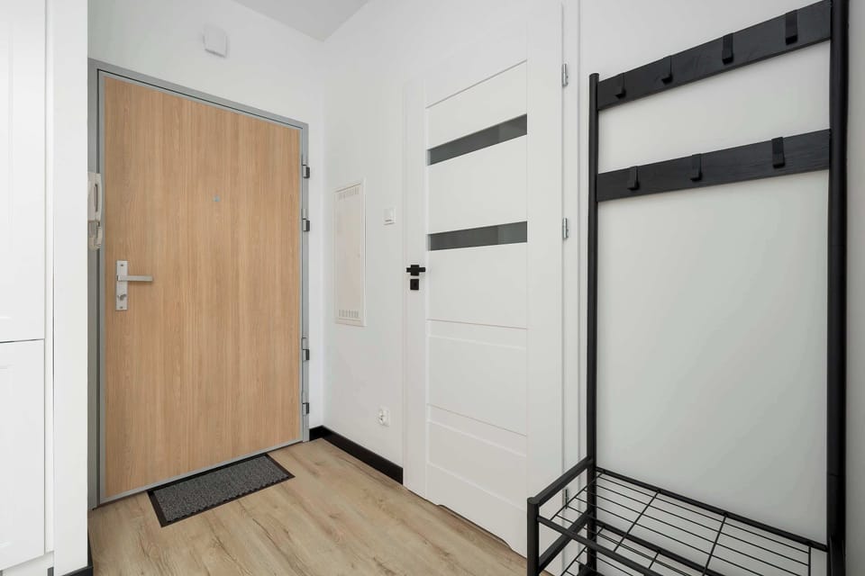 The apartment entrance hallway features a light wood-look door, a clothing rack, and an intercom system. The clean lines and functional layout provide a welcoming first impression.