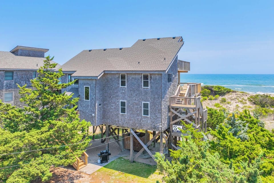 Coastal retreat elevated on stilts with ocean views, surrounded by natural dune vegetation and direct beach access via private walkway.