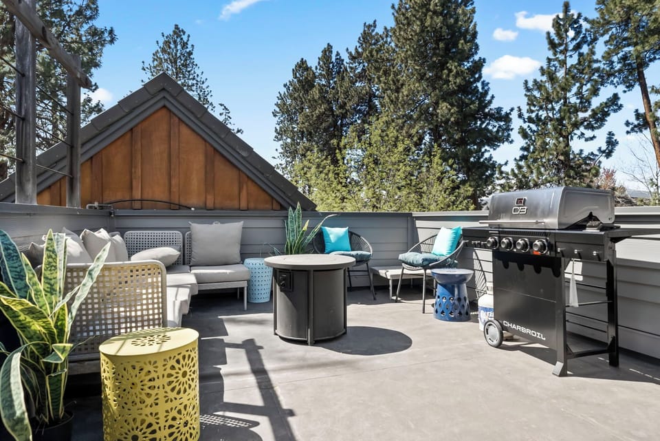 Your private rooftop retreat combines mountain living with modern comfort, featuring plush seating, a stylish fire table, and a premium gas grill surrounded by towering pines under open skies.