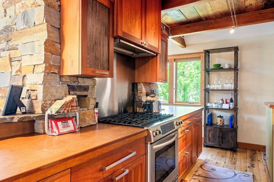 Cook your favorite meals in this well-equipped kitchen featuring rich wood cabinetry, a gas stove, and stunning stone fireplace that adds rustic charm to your mountain getaway.