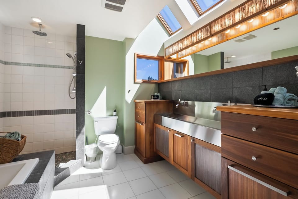 Freshen up in your spacious bathroom featuring a rainfall shower, sleek fixtures, and natural light streaming through skylights. Warm wood cabinetry and soft towels await your arrival.