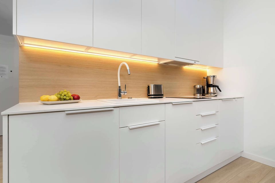 A line of white kitchenette cabinets with LED under-cabinet lighting creates a functional and modern cooking space. A wood-like panel above the countertop adds natural charm to the interior.
