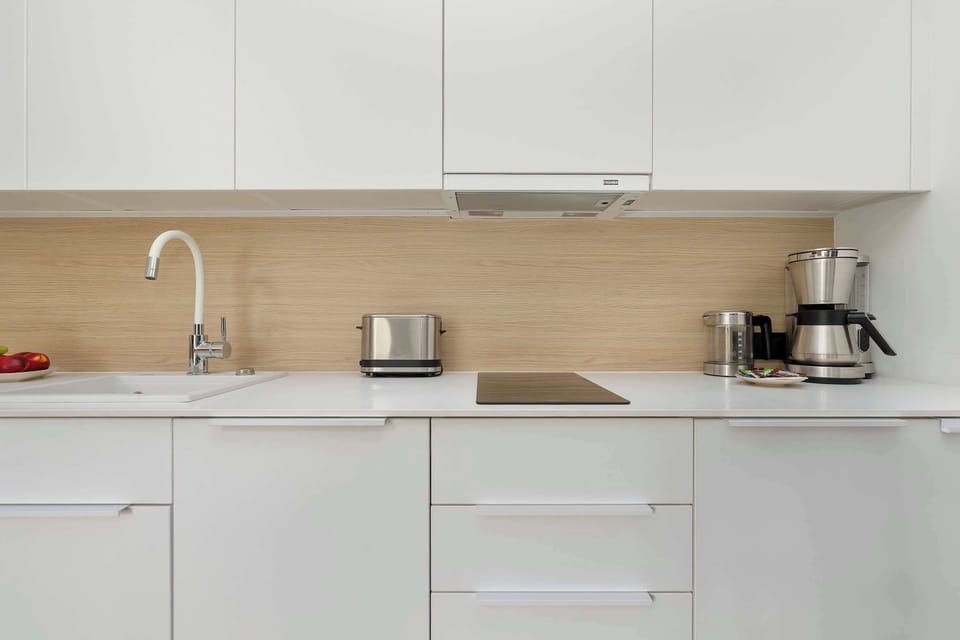 A close-up of the kitchenette workspace shows a built-in hob, a toaster, and a coffee maker. The bright cabinet fronts harmonise perfectly with the chrome kitchen faucet.