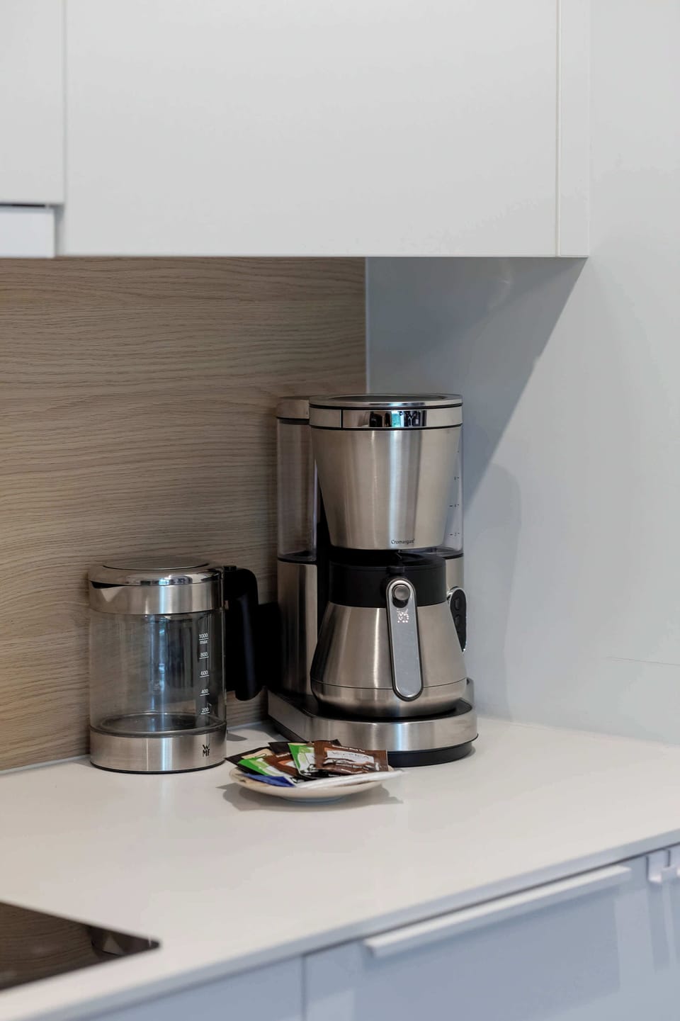 A detailed shot of the kitchen counter presents a modern stainless-steel filter coffee machine and a matching toaster. The minimalist arrangement focuses on aesthetic and practical accessories.