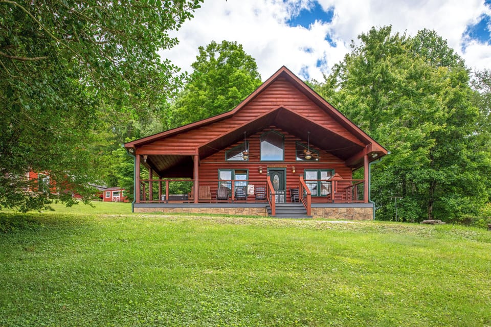 A charming log cabin nestled in lush greenery, offering a peaceful retreat with a spacious wraparound porch perfect for morning coffee and evening relaxation surrounded by nature.