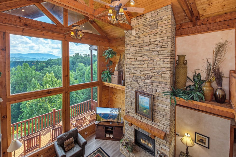 Settle into your cozy living room where floor-to-ceiling windows frame stunning mountain and forest views. The stone fireplace adds warmth while natural light pours through the soaring vaulted ceilings.