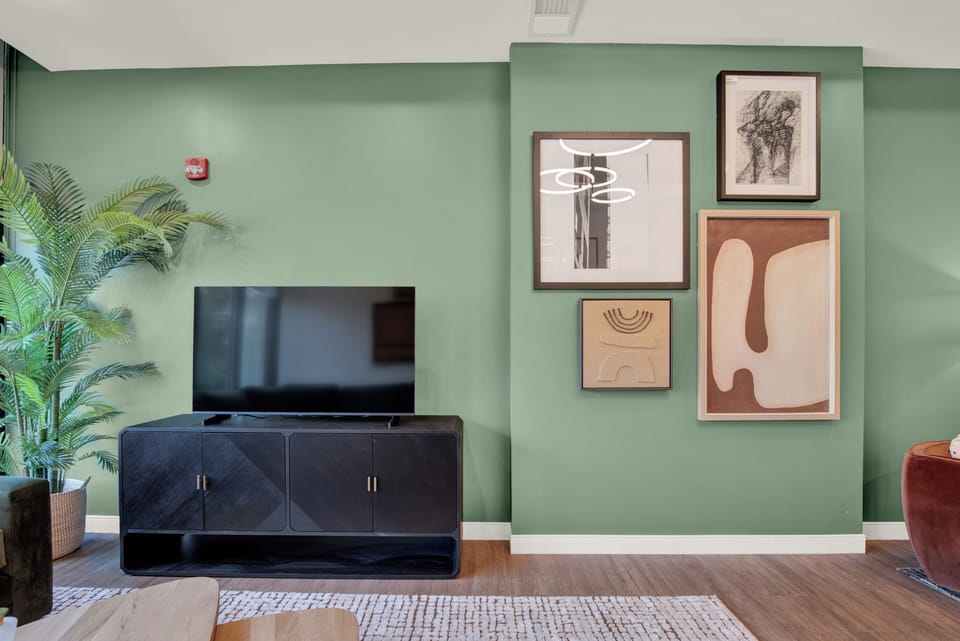 Stylish lounge with sage accent wall, art gallery display, and large TV