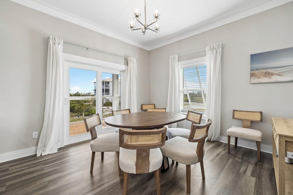 Gather around this inviting dining table, where natural light pours through large windows and a coastal art piece sets a serene tone for your meals together.