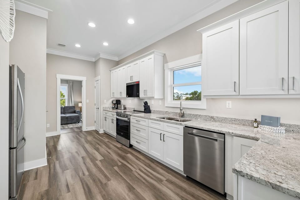 Bright, modern kitchen with granite countertops and stainless steel appliances ready for your culinary adventures. White cabinetry and wood-style flooring create a fresh, inviting space.