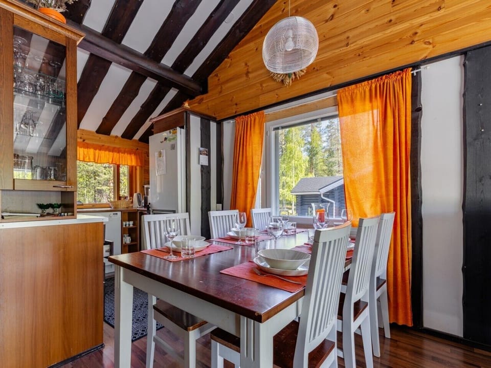 The dining room comfortably seats the group around a solid wood table, with bright orange curtains framing the forest outside.