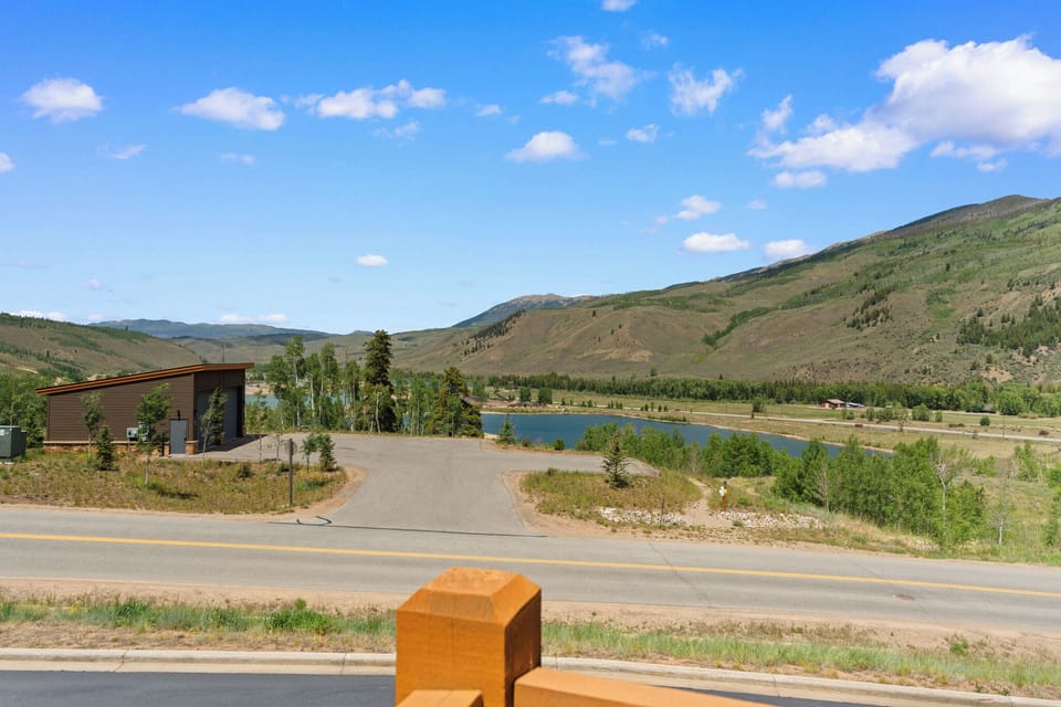 Modern mountain retreat nestled in a serene valley landscape, with river views and rolling foothills framing this peaceful natural setting under expansive blue skies.