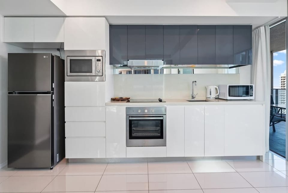 Prepare delicious meals in this modern, fully equipped kitchen featuring sleek grey upper cabinetry, crisp white base units, integrated stainless steel appliances, and a full-size refrigerator.