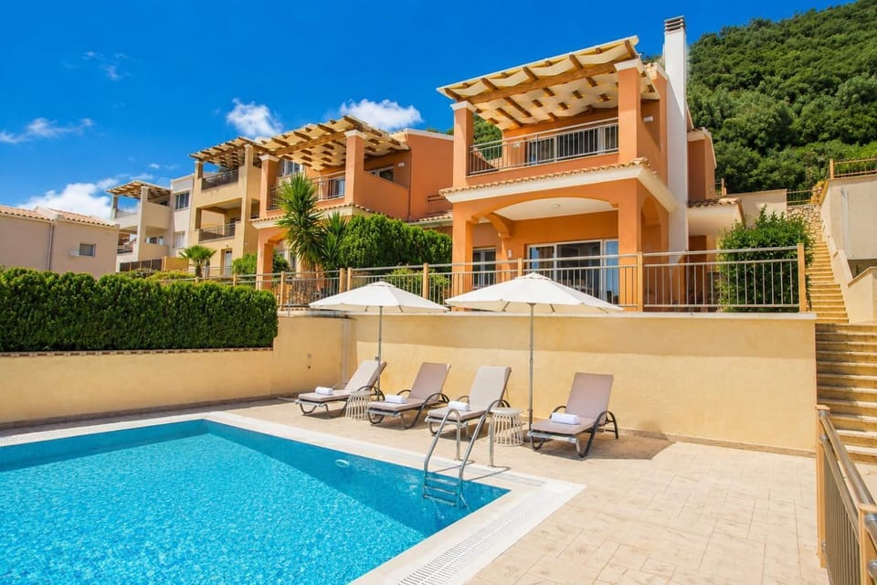 Sunny pool terrace with comfortable sun loungers, white umbrellas, and a lovely villa backdrop.