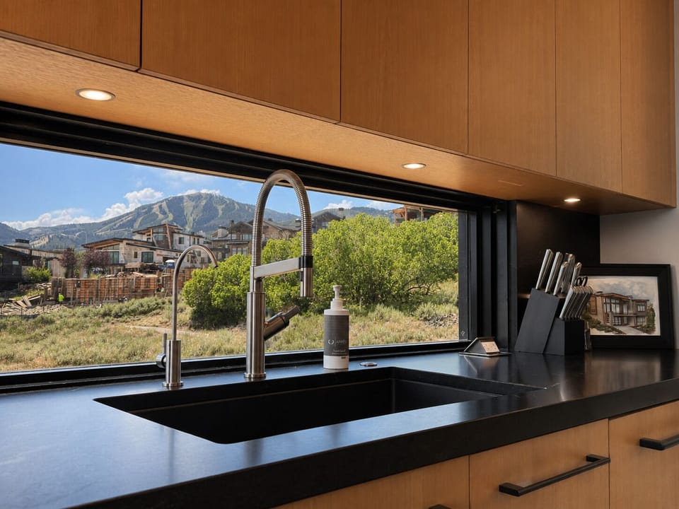 Even everyday moments feel elevated with a beautifully finished kitchen sink positioned beneath a large picture window overlooking the surrounding mountains and neighborhood.