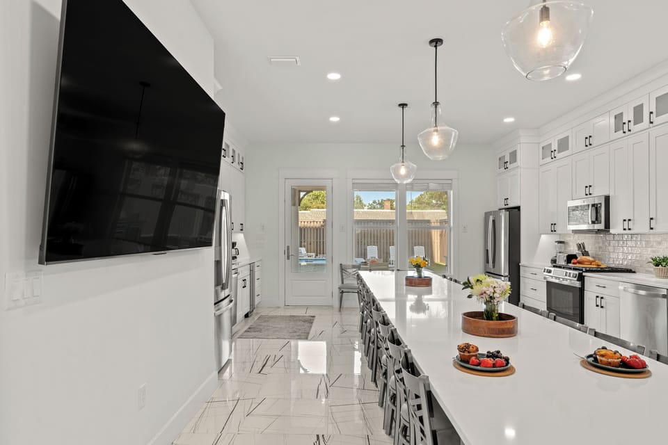 Sleek linear view highlighting the grand kitchen island, modern lighting fixtures, and patio exit.