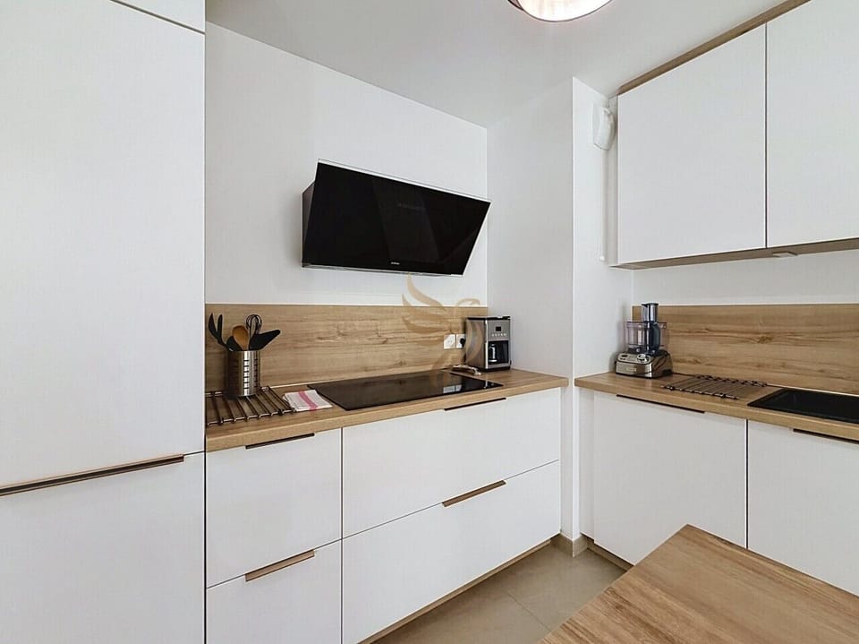 Le matin, la cafetière chauffe sur le plan en bois tandis que la plaque induction attend votre omelette : une cuisine épurée où design blanc et touches bois rendent chaque préparation accueillante et simple.