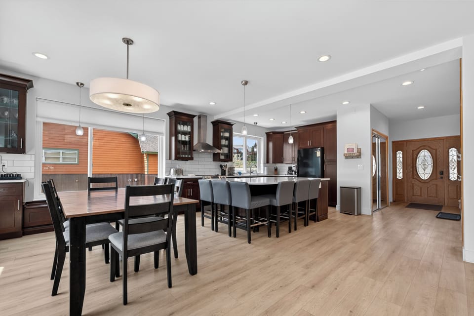 A spacious open-concept kitchen and dining area featuring rich dark cabinetry, a large island with bar seating, elegant pendant lighting, and warm wood flooring—perfect for gathering and entertaining.