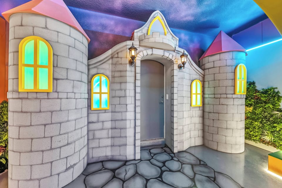 Step into a whimsical entrance that feels like a fairytale, complete with charming castle-like towers and vibrant colored windows. The textured stone pathway leads the way, inviting you to explore the enchanting atmosphere within.