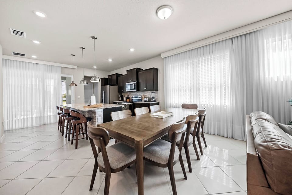 Enjoy family meals in this bright and spacious dining area, featuring a large wooden table and sleek chairs. Natural light floods the space, accentuating the modern kitchen with its rich cabinetry and stainless appliances.