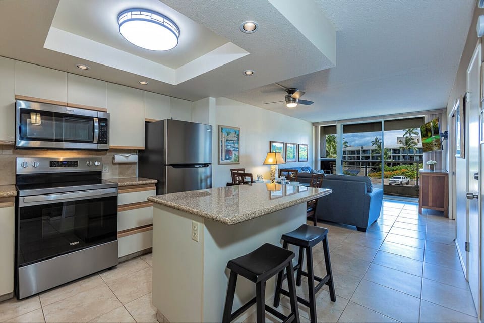Your bright, open-concept space flows seamlessly from the kitchen with stainless steel appliances to the inviting living area with tropical views beyond.