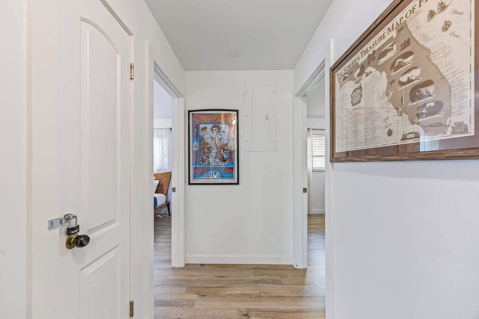 Hallway with framed artwork and access to adjacent bedrooms featuring natural light and wood flooring.