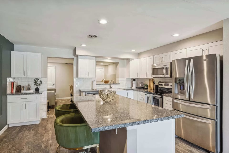 The kitchen impresses with a large granite island with seating for 2, farmhouse sink, white shaker cabinets, tile backsplash, Keurig coffee maker, and full stainless steel appliance suite.