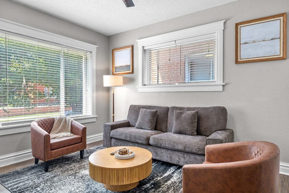 A sofa, two leather accent chairs, round coffee table, and two large windows create a bright living-room seating area.