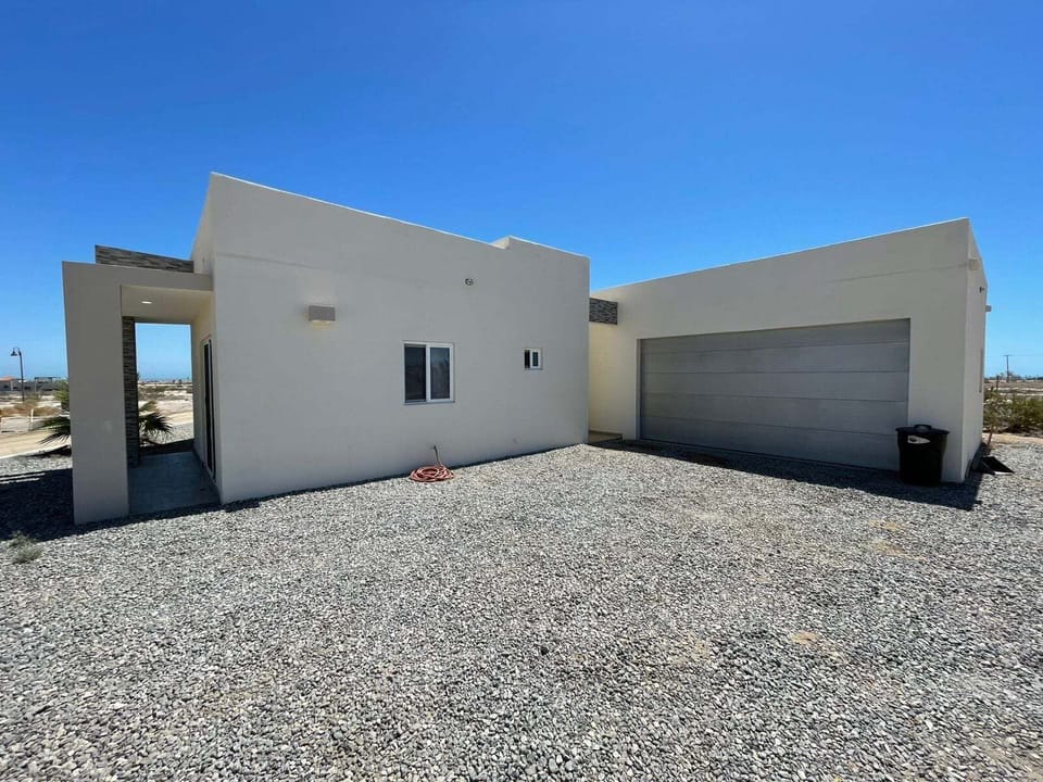 An exterior perspective captured from the right rear side of the property, showcasing the deep architectural profile of the complex, the clean stucco finishes, and a clear view of the secure garage entrance and spacious driveway access.