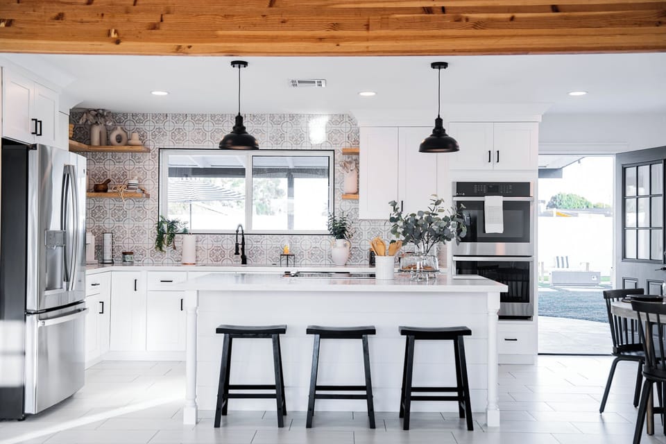 Chef's kitchen showcasing a massive central island with breakfast bar seating, custom tile backsplash, and statement black pendant lighting.