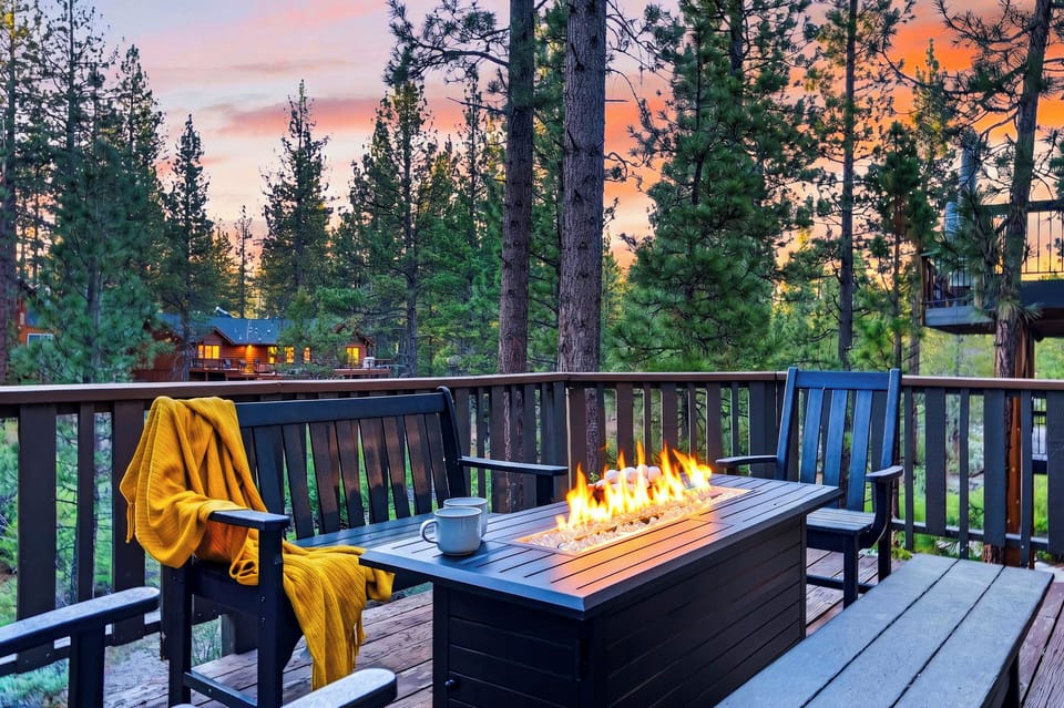 Cozy deck seating with a fire table, sunset skies, and peaceful pine views.