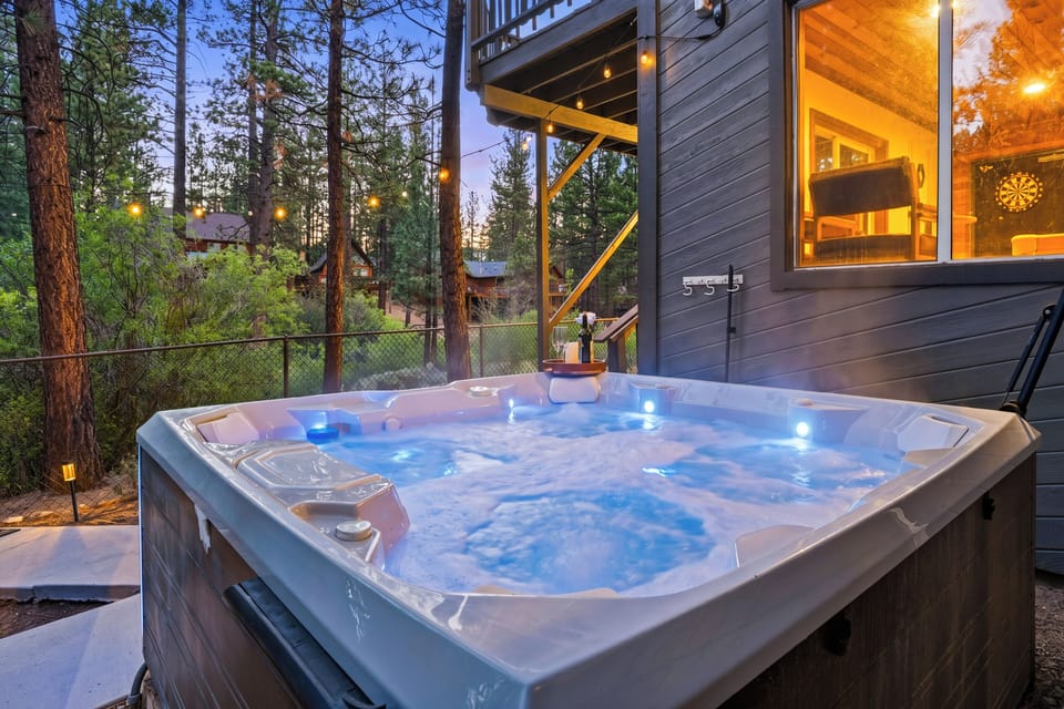 Private hot tub tucked beneath the deck with string lights and peaceful pine views.